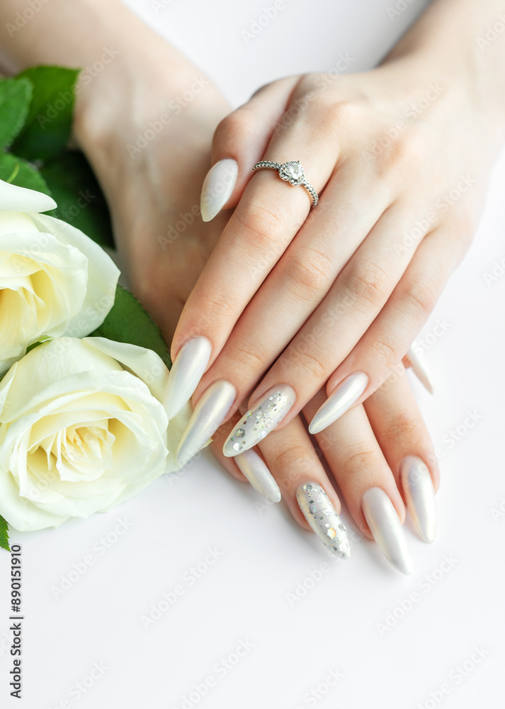 Fototapeta premium Female Hands on a white background with beautiful pearl manicure and white roses.