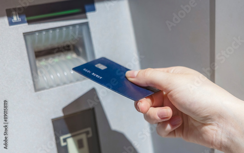 A women’s hand inserts a blue credit card into an ATM card reader. Women’s hand with manicure and a banking card.
