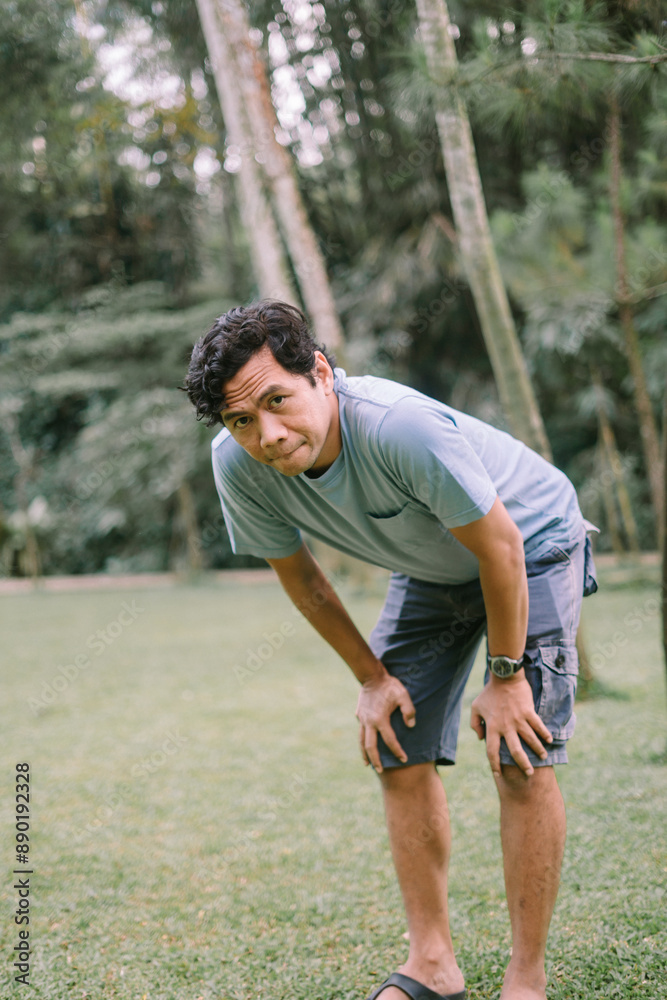 A Southeast Asian man bending over and holding his knees, capturing a moment of exhaustion or effort