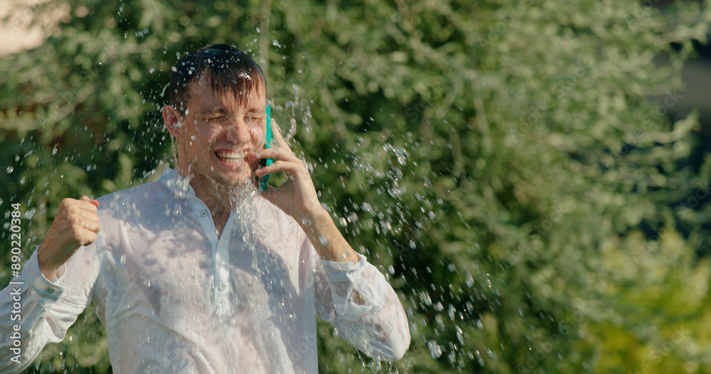 A man getting splashed with water while talking on the phone A man getting splashed with water while talking on the phone