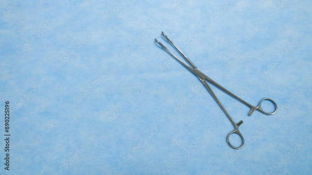 Fototapeta premium Sponge holding forceps are used during surgical procedures to hold sponges and swabs. Medical Equipment used by surgeons in surgery placed on a blue background.