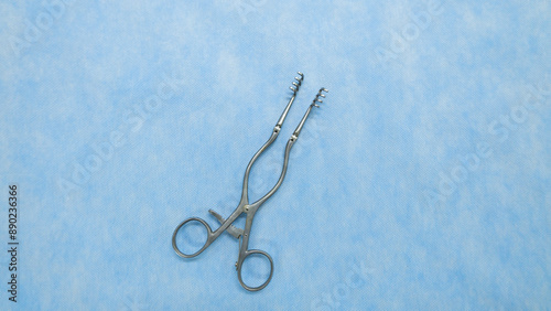 A Weitlaner self-retractor used in heart surgery placed on a blue background. Medical instruments used in the operating room. Surgical clamp with retainer. photo