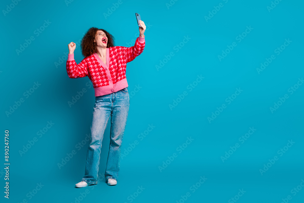 Full length photo of shiny lucky lady dressed red cardigan rising fist recording video gadget empty space isolated blue color background Full length photo of shiny lucky lady dressed red cardigan rising fist recording video gadget empty space isolated blue color background