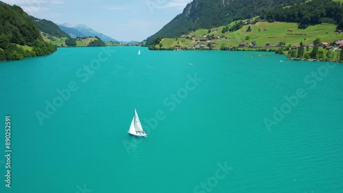 Drone footage of turquoise clear lake Lungern or Lungerersee in Switzerland in summer sunny day with village and green meadow
