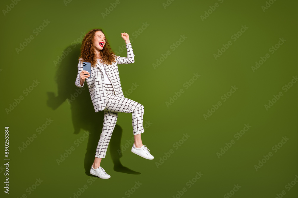 Photo portrait of attractive young woman hold device win celebrate dressed stylish white plaid clothes isolated on khaki color background Photo portrait of attractive young woman hold device win celebrate dressed stylish white plaid clothes isolated on khaki color background