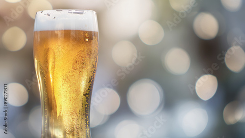 Glass of cold beer with foam on a blurred background of warm bokeh lights. The condensation on the glass highlights the refreshing nature of the beverage