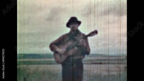 Musician portrait, walk through field nature, sing songs. Music artist performance on natural meadow background. Romantic man play guitar in summer outdoors. Vintage color film. Retro 1960s archive