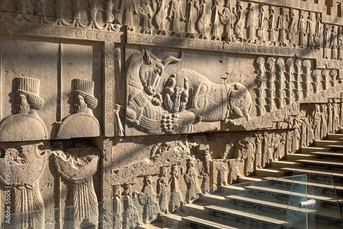 Bas-relief carvings of a lion hunting a bull beside embossed soldiers on one of the staircases in Persepolis, a UNESCO World Heritage site located in northeast of Shiraz, Iran