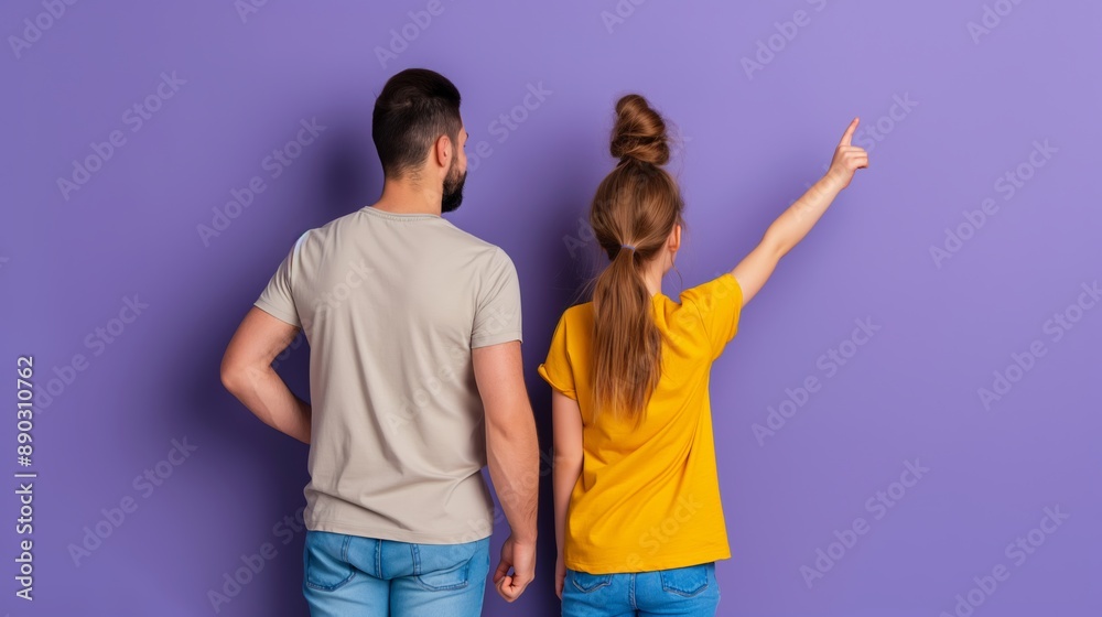 Obraz premium A man and a woman are standing next to each other pointing at something. The man is wearing a gray shirt and the woman is wearing a yellow shirt. Scene is lighthearted and playful