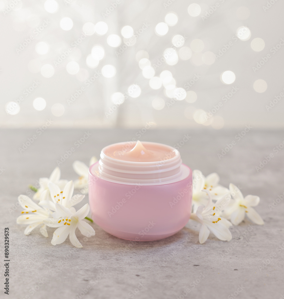 Cream in jar and beautiful jasmine flowers on grey table against light background with blurred lights, closeup Cream in jar and beautiful jasmine flowers on grey table against light background with blurred lights, closeup