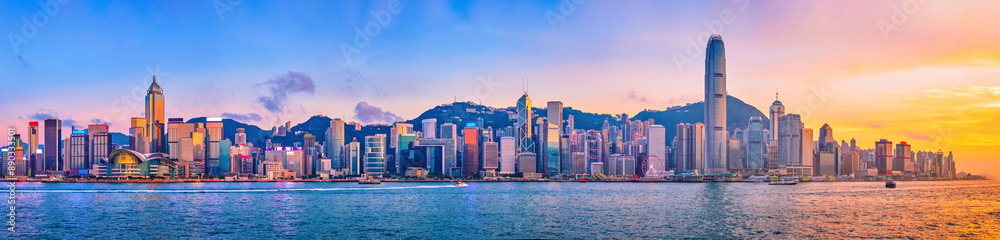 Naklejka premium Panorama of Hong Kong skyline cityscape downtown skyscrapers over Victoria Harbour in the evening with junk tourist ferry boat on sunset with dramatic sky. Hong Kong, China