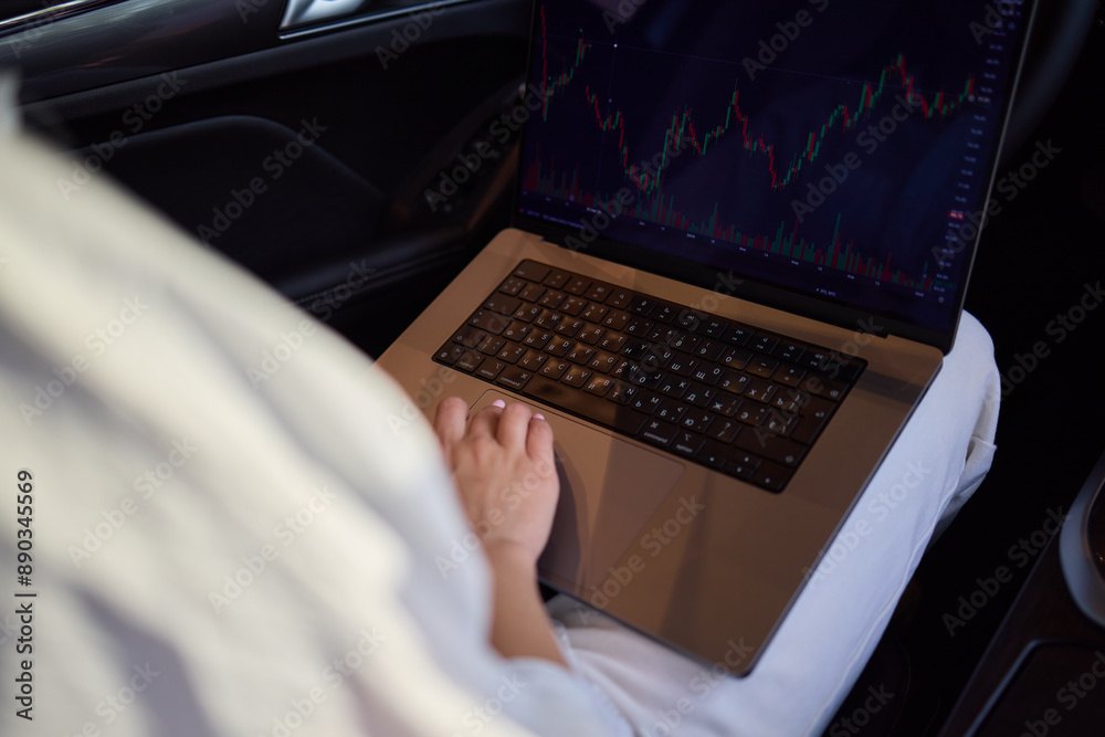 Fototapeta premium A person is working on a laptop inside a car during their commute to a destination