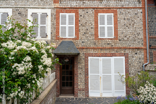 An empty yard of a classic stone house with closed shutters and flowering bushes. The concept of a quiet peaceful life in Western Europe.