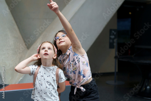 Two cute beautiful schoolgirls look up with surprise and interest in the museum. Children's education concept