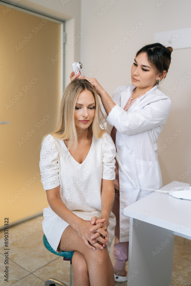 Vertical shot of female trichologist making diagnosis of structure and condition of blonde woman hair with special device trichoscope in dermatological clinic. Concept of hair care and treatment. Vertical shot of female trichologist making diagnosis of structure and condition of blonde woman hair with special device trichoscope in dermatological clinic. Concept of hair care and treatment.
