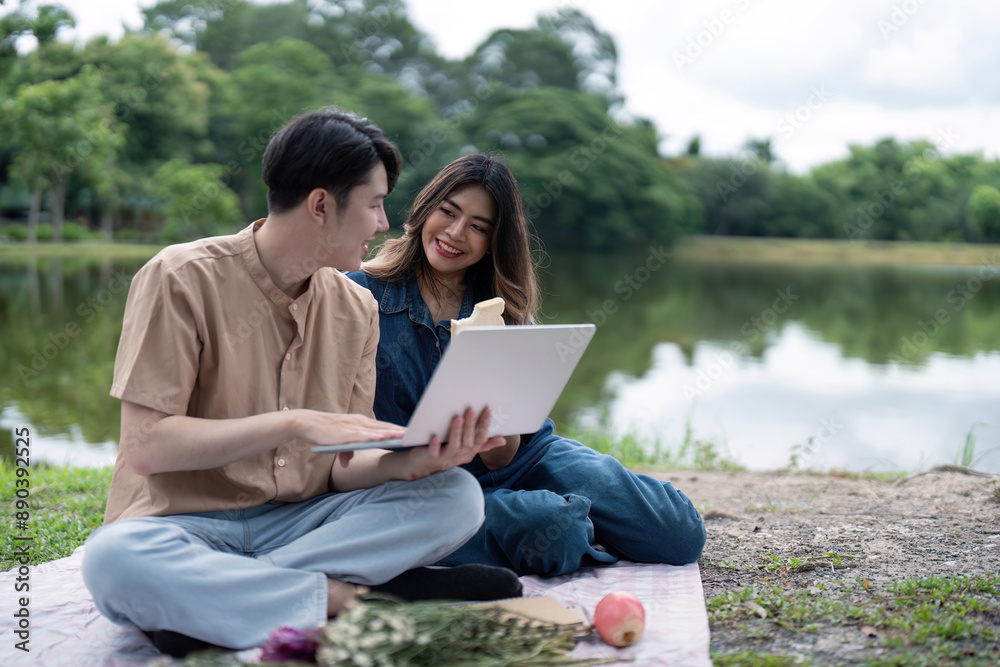 Young Couple Enjoying a Relaxing Picnic by the Lake with a Laptop on a Beautiful Day Young Couple Enjoying a Relaxing Picnic by the Lake with a Laptop on a Beautiful Day
