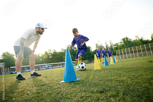 Obraz na plátne Young boy, child in motion, dribbling soccer ball around cones and receiving guidance from coach