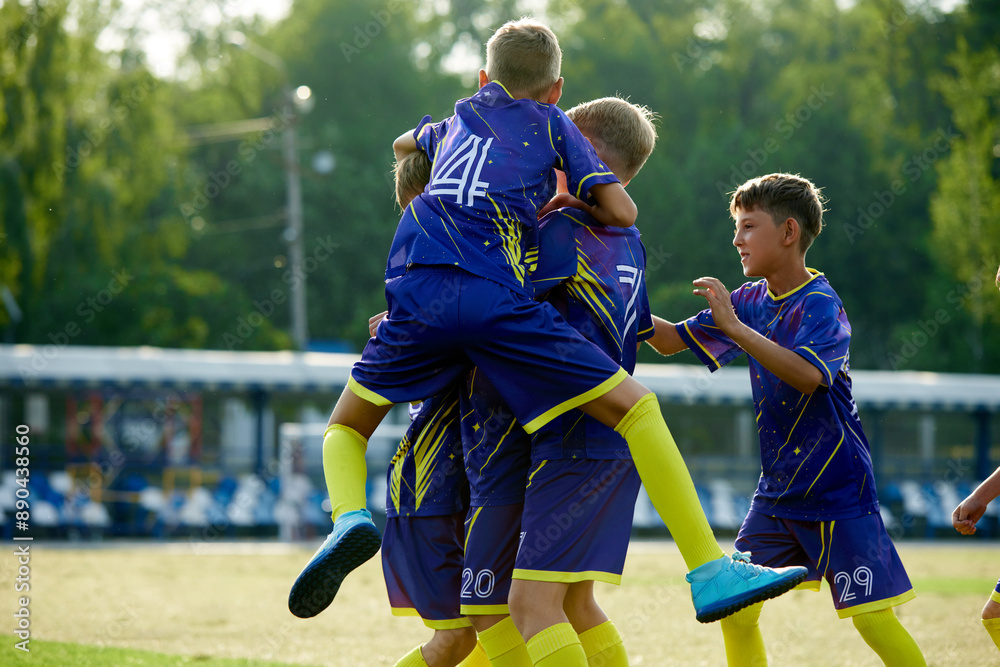 Obraz premium Dynamic moment of victory. Boys, friends in blue uniform, soccer players in motion, jumping and hugging, celebrating winning game. Concept of sport, childhood, education, achievement, active lifestyle
