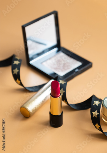 A shot of red lipstick with make up palette and black ribbon with dark orange color isolated background 