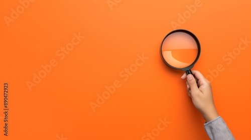 A hand holding a magnifying glass over a orange background with copy space, the concept of searching for information or finding a job candidate	
