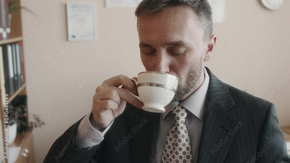 Tilt closeup of happy bearded Caucasian employer in black striped suit enjoying nice cup of tea, inhaling its aroma and sipping it during break in retro office, 90s Tilt closeup of happy bearded Caucasian employer in black striped suit enjoying nice cup of tea, inhaling its aroma and sipping it during break in retro office, 90s