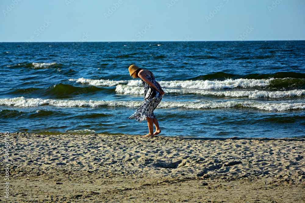dziewczyna w kapeluszu na plaży szukajaca muszelek, schylona dziewczyna na tle morza, a girl in a hat on the beach looking for shells, a girl bending over against the background of the sea,