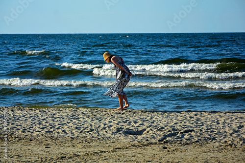 Obraz na płótnie dziewczyna w kapeluszu na plaży szukajaca muszelek, schylona dziewczyna na tle morza, a girl in a hat on the beach looking for shells, a girl bending over against the background of the sea, w salonie