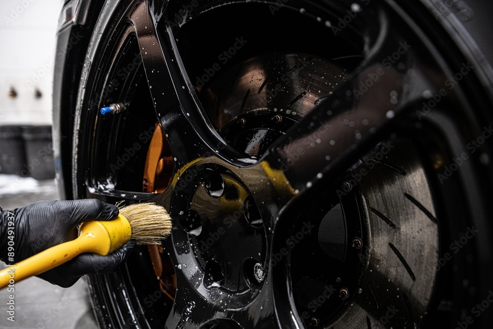 Detailing car wheel using brush for thorough cleaning. Focus on precision and high-quality finish in professional auto detailing, ensuring spotless and shiny wheels