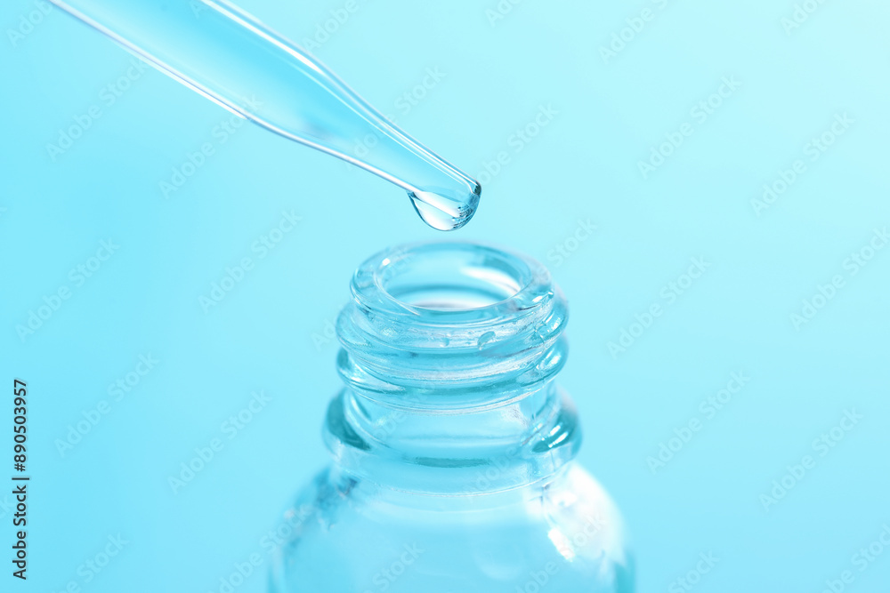 Dripping liquid from pipette into glass bottle on light blue background, closeup