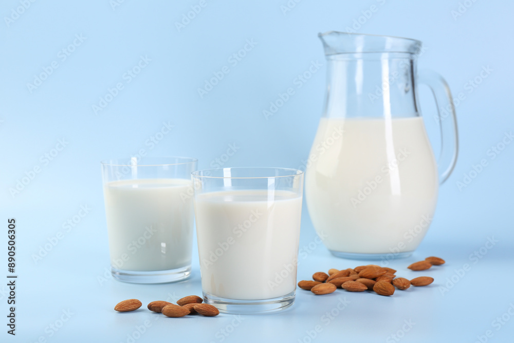 Fresh almond milk in glasses, jug and nuts on light blue background Fresh almond milk in glasses, jug and nuts on light blue background