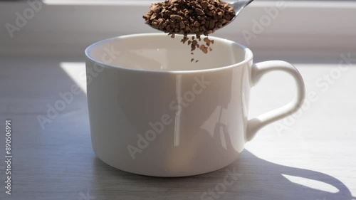 Pour instant coffee into a coffee cup in slow motion. Sprinkle instant coffee beans with a spoon