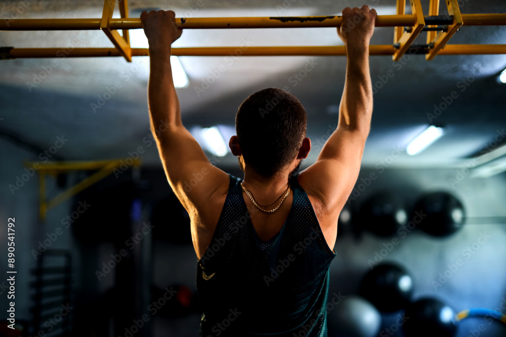 Naklejka premium Back view of a strong man doing pull ups in a gym