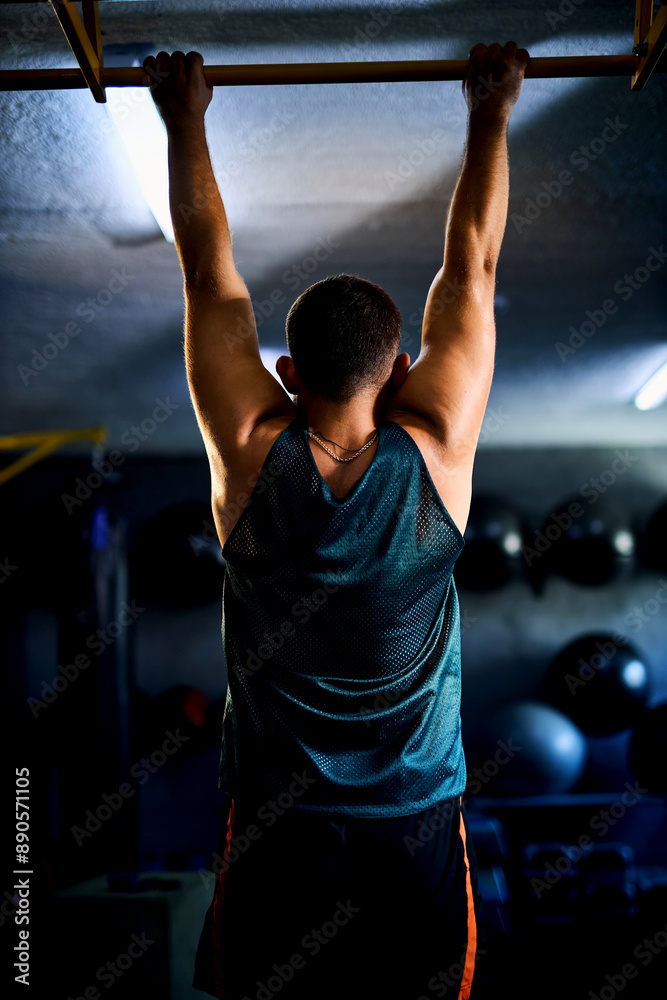 Fototapeta premium Back view of a strong man doing pull ups in a gym