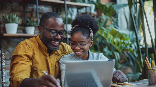 A father helping his cheerful teenage daughter with homework at home, both smiling and working together on a laptop photo