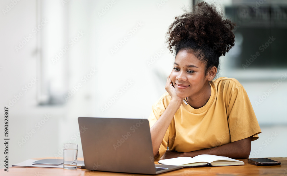 Business And Education Concept. Smiling young black woman student sitting at desk watching on laptop, free copy space. Happy millennial female studying using pc Business And Education Concept. Smiling young black woman student sitting at desk watching on laptop, free copy space. Happy millennial female studying using pc