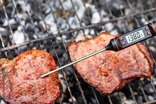 Close-up shot of digital meat thermometer inside grilled steak on barbecue showing the right temperature for Medium doneness photo