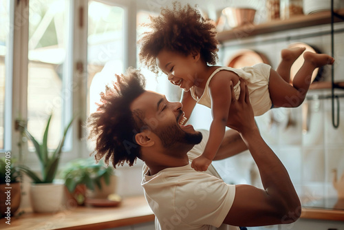 african american dad having fun with his daughter flying in the air in a kitchen photo