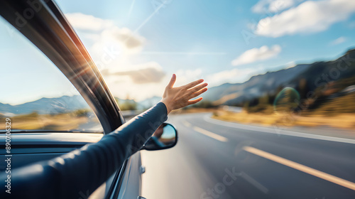 A person extends their hand out of a car window while driving on a scenic road during a sunny day, capturing a sense of freedom and adventure.