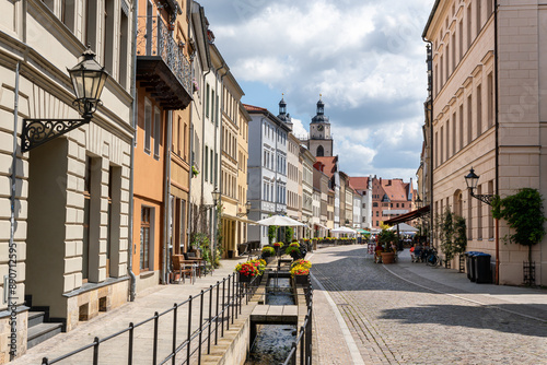 View along the castle street in Wittenberg, Saxony-Anhalt. In the distance the market square and the town church of St. Mary in Wittenberg. Small shops decorated with flowers.