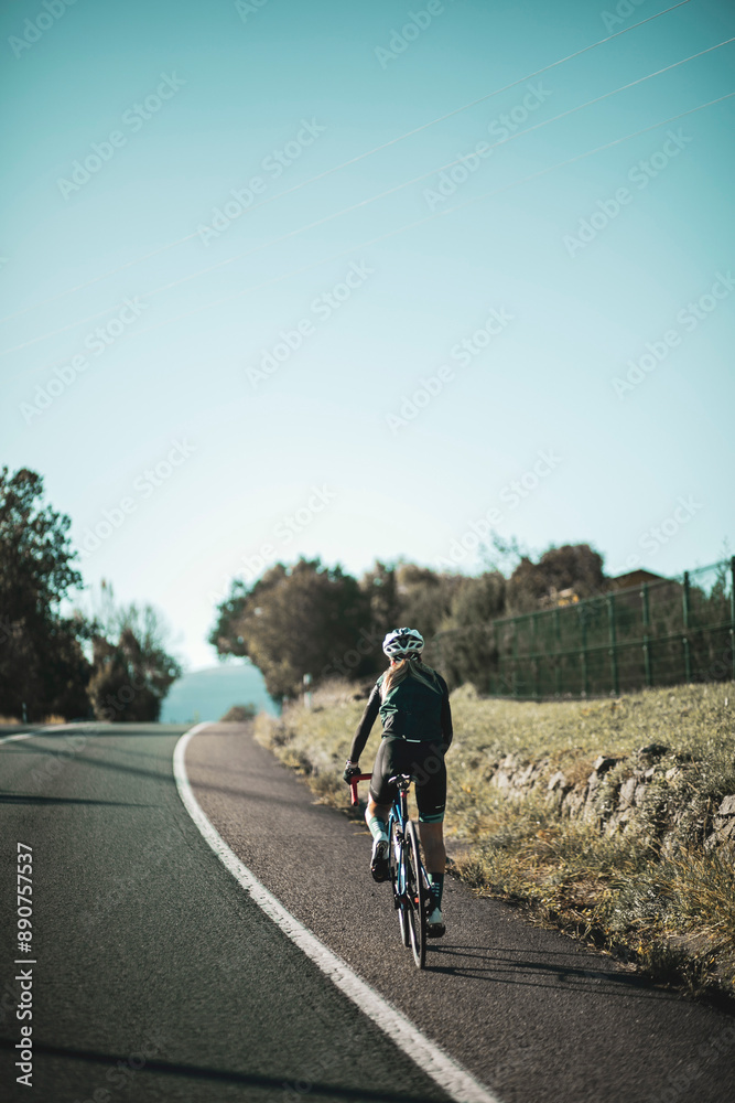 A woman cyclist training on a lonely road on a sunny day wearing a black jersey and bib shorts and a white helmet. A woman cyclist training on a lonely road on a sunny day wearing a black jersey and bib shorts and a white helmet.