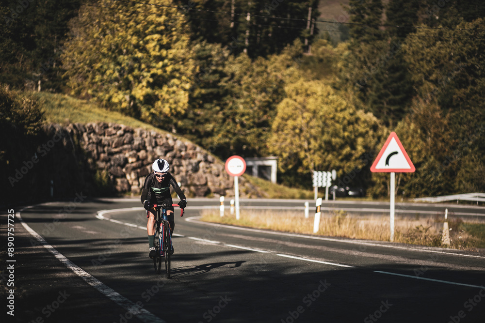 A woman cyclist training on a lonely road on a sunny day wearing a black jersey and bib shorts and a white helmet. A woman cyclist training on a lonely road on a sunny day wearing a black jersey and bib shorts and a white helmet.