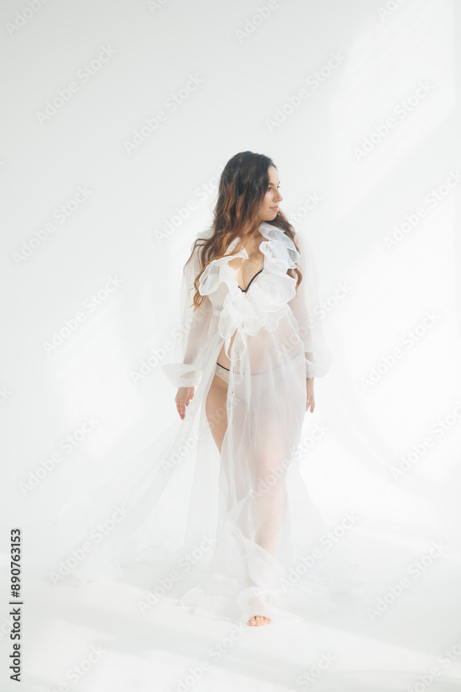 A beautiful pregnant brunette woman in a white flying transparent negligee, dressing gown. A pretty girl with a bare stomach in lingerie stay barefoot on a white background. Smile, portrait A beautiful pregnant brunette woman in a white flying transparent negligee, dressing gown. A pretty girl with a bare stomach in lingerie stay barefoot on a white background. Smile, portrait