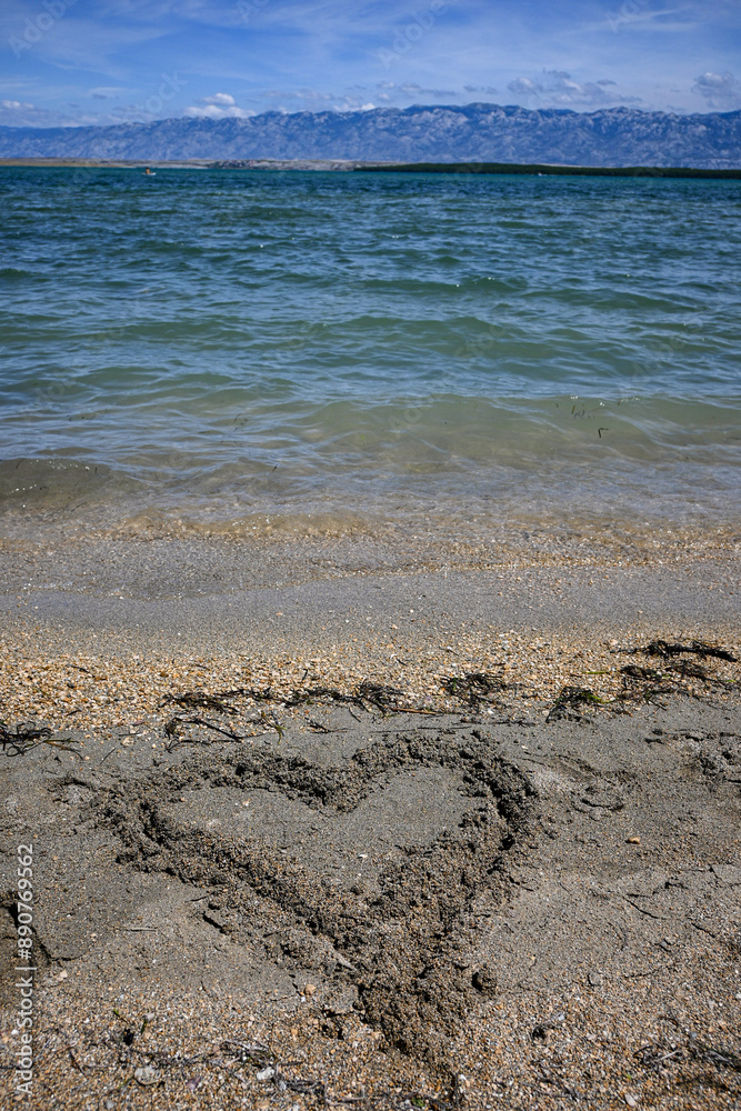 Heart drawn in the sand on a beach being washed away by the ocean waves, representing lost love