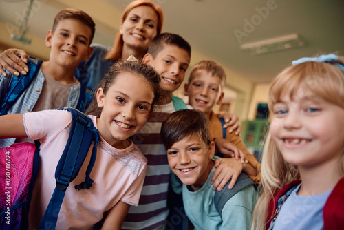 Happy school kids and their teacher in classroom looking at camera.