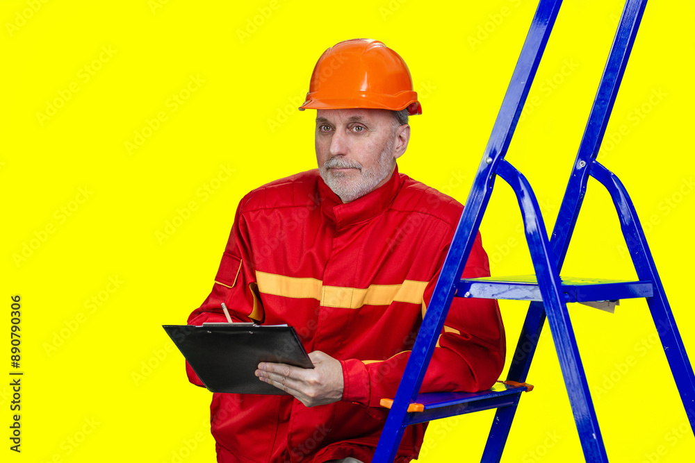 Mature caucasian contruction worker with clipboard and pencil. Isolated on yellow. Mature caucasian contruction worker with clipboard and pencil. Isolated on yellow.