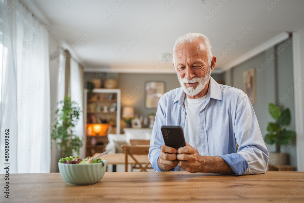 Senior man use a mobile phone while eat salad at home Senior man use a mobile phone while eat salad at home