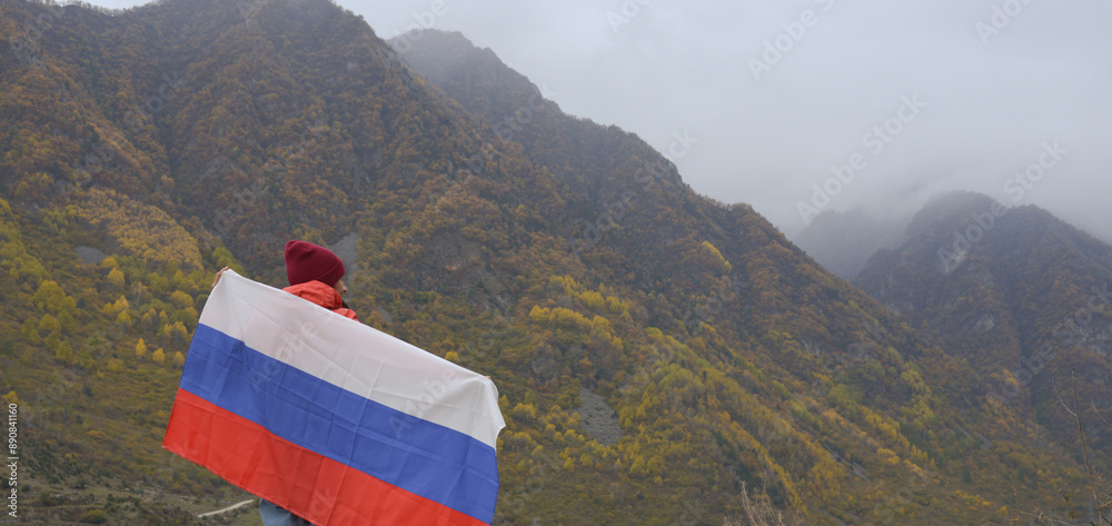 The flag of Russia flutters beautifully behind a woman's back against the backdrop of mountains on a cloudy day. Close-up rear view. Russian Independence Day
