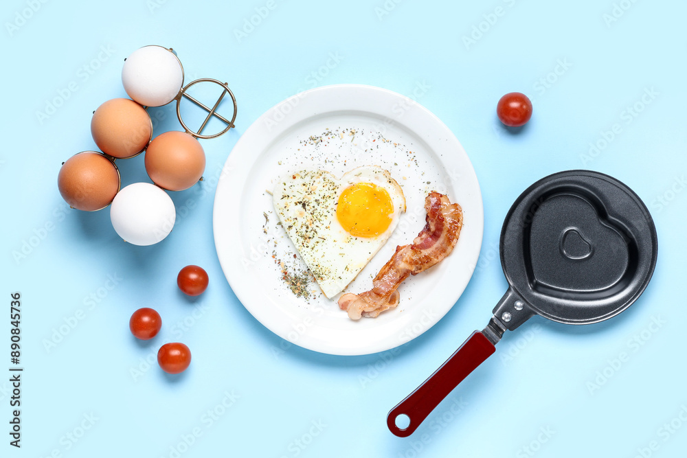 Composition with frying pan, heart-shaped fried egg and ingredients on blue background Composition with frying pan, heart-shaped fried egg and ingredients on blue background