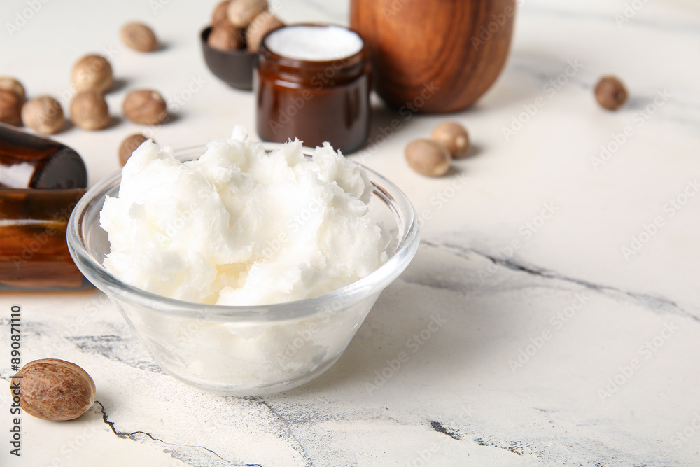 Fototapeta premium Glass bowl of shea butter and nuts on white background