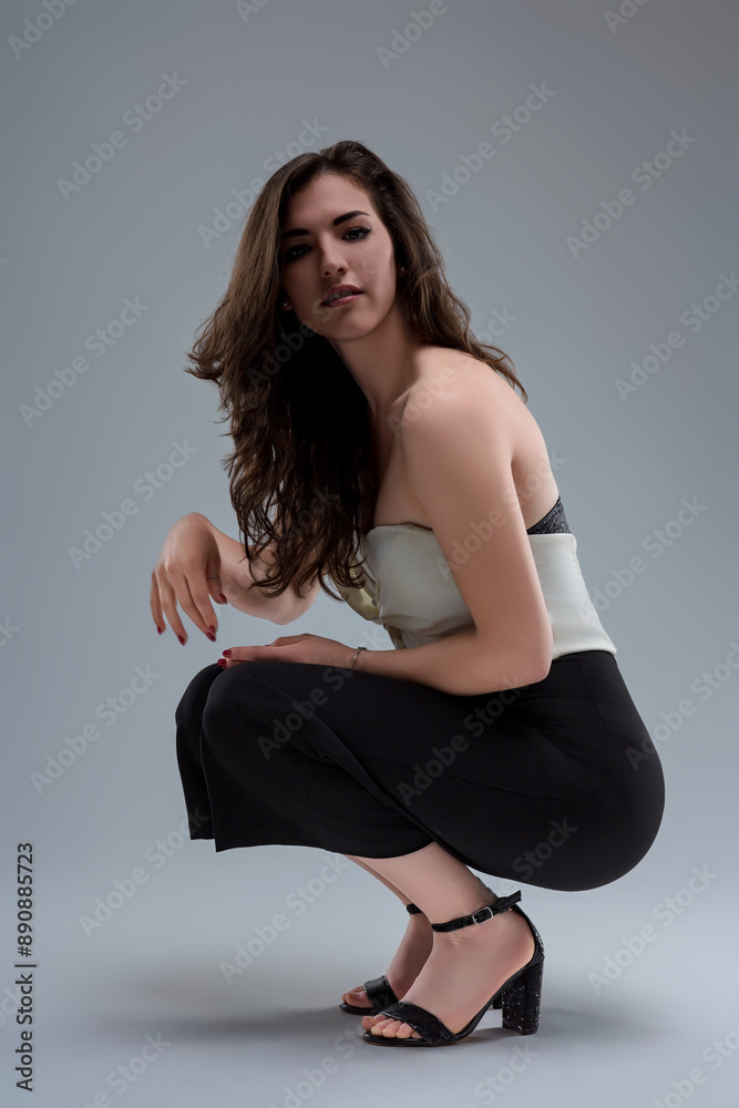 Young woman wearing white top and black pants crouching in studi Young woman wearing white top and black pants crouching in studi